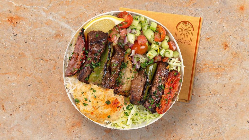 Beef Skewer Rice Bowl · Grilled beef over basmati rice with hummus, diced cucumber and tomato salad, shredded green cabbage and a drizzle of tahini sauce.