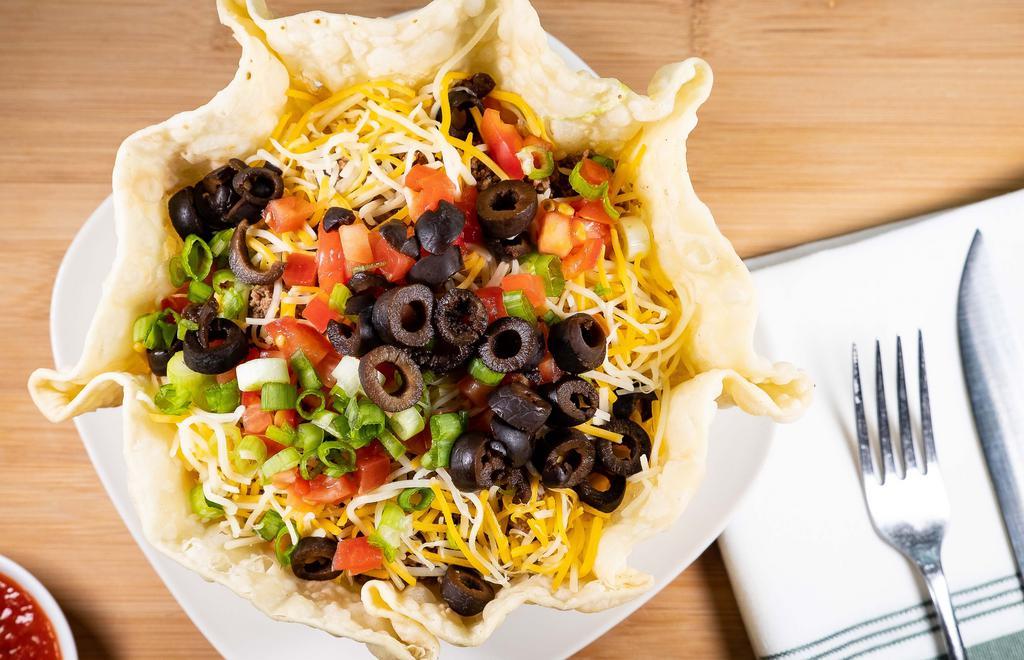 Taco Salad · A crispy tortilla bowl filled with shredded lettuce, ground beef or shredded chicken, mixed cheese, tomatoes, green onions, black olives, and a side of sour cream.