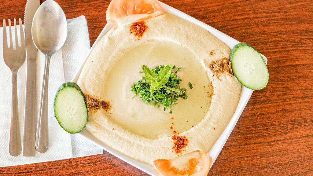 Hummus · A creamy dip of garbanzo beans, tahini, garlic, lemon and drizzled with olive oil, served with pocket bread.