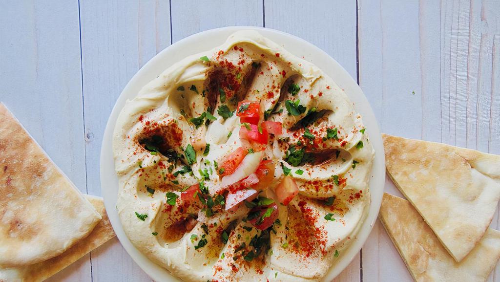 Hummus · A Middle Eastern spread made from chickpeas topped with extra virgin olive oil, paprika, tomatoes and onions.