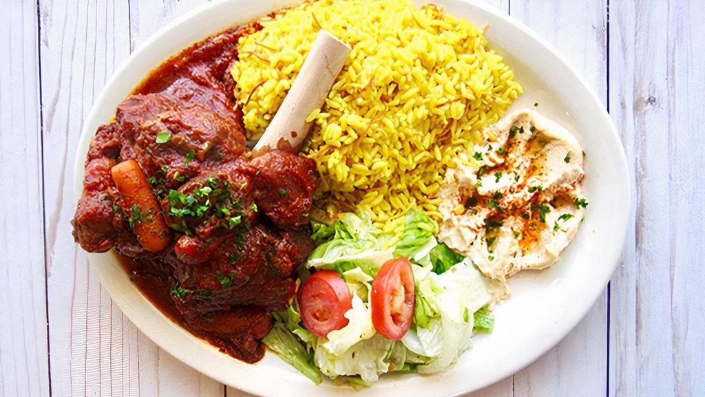 Lamb Shank Dinner · Mediterranean spiced braised lamb shank,
cooked in a red wine and tomato sauce with vegetables, aromatics and fresh herbs. Served with rice, hummus, salad and vegetables.