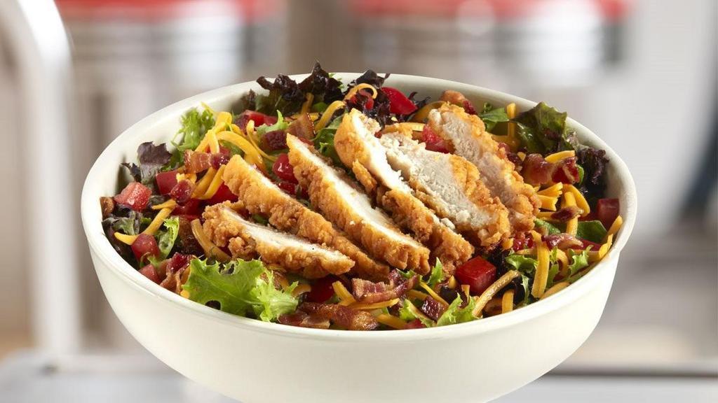 Crispy Chicken Club Salad · A crispy take on the salad style club featuring lightly breaded chicken tenders on a bed of seasonal greens, topped with crumbly bacon, diced tomatoes, shredded cheddar and your choice of dressing.