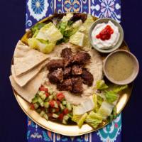 Beef Kabob Hummus Platter · Beef kabob served over hummus with salad, grilled tomatoes, pita, and your choice of sauce.