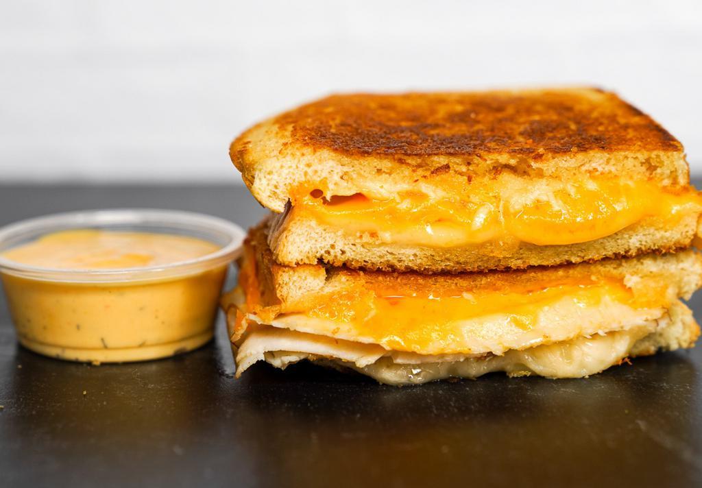Three Cheese Grilled Cheese · Cheddar, Swiss, and Parmesan cheeses melted between buttery, toasted sourdough bread. Served with a side of Spicy Honey Mustard Aioli.