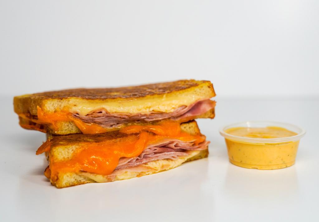 Smoked Ham And Cheese Monte Cristo · Smoked ham, Cheddar, Swiss, and Parmesan cheeses melted between egg dipped, griddled sourdough bread. Served with a side of Spicy Honey Mustard Aioli.