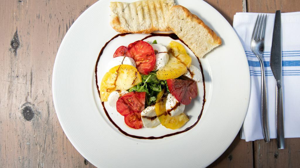 Insalata Caprese (Vegetarian) · This dish contains sliced mozzarella fiordilatte,  large heirloom tomatoes, and arugula which are lightly seasoned with extra virgin olive oil and a balsamic glaze.  This dish also comes with 2 pieces of artisanal focaccia (bread).  Serves 1-2 people as an appetizer.