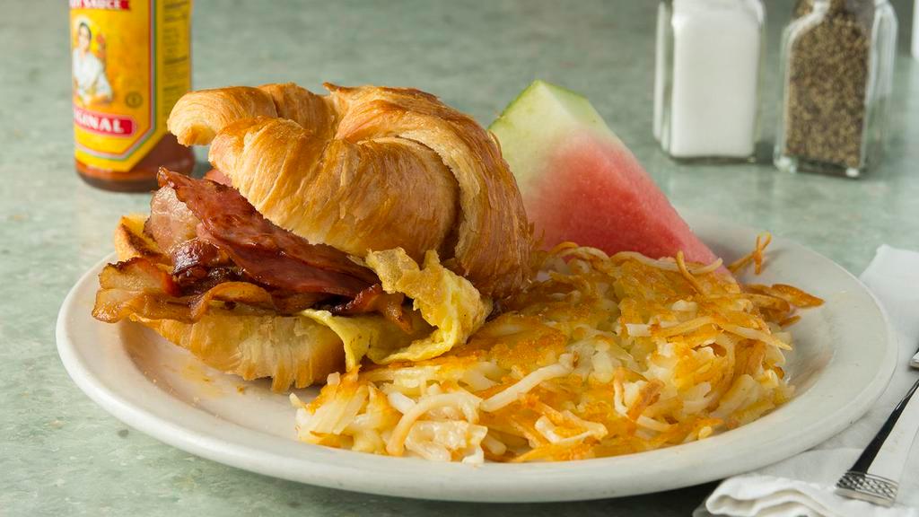 Breakfast Sandwich · A grilled croissant with two fresh eggs scrambled with a choice of  bacon, ham, or sausage, and topped cheese. served with fruit.
