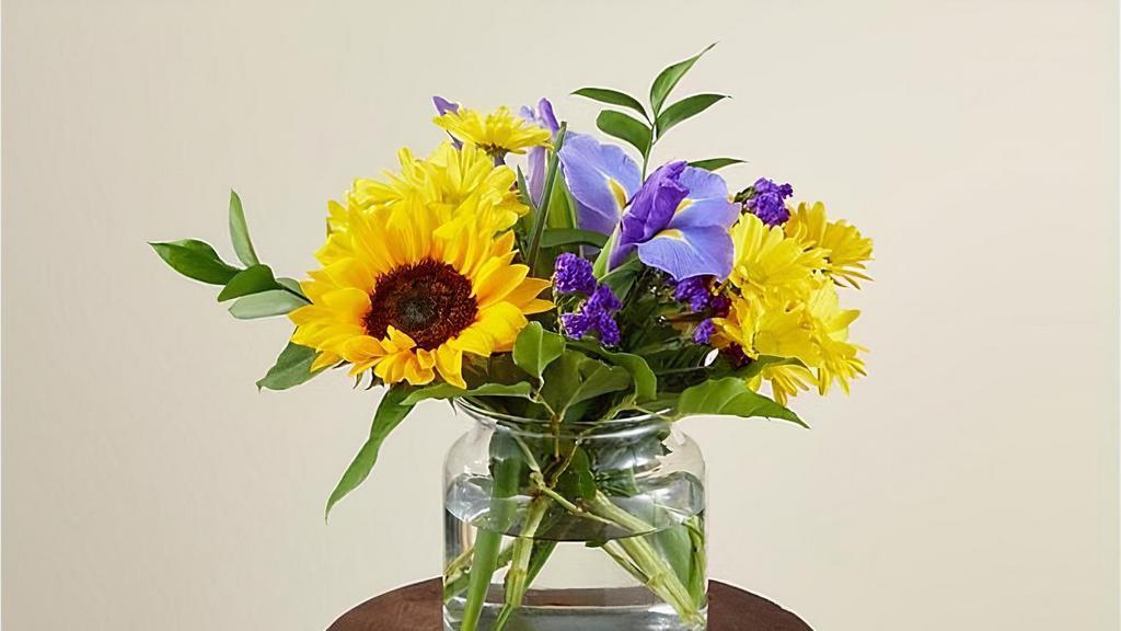 Flutter By · The cheerful Flutter By Bouquet is guaranteed to make every recipient smile. Designed with energetic yellow sunflowers and daises that are beautifully contrasted by blue iris. This arrangement is the perfect addition to a surprise birthday party or just a 'thinking of you' gift. Vase included. Please Note: The bouquet pictured reflects our original design for this product. While we always try to follow the color palette, we may replace stems to deliver the freshest bouquet possible. Item # M2S