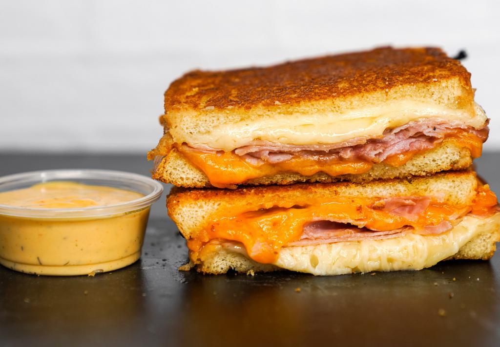 Smoked Ham & Three Cheese Melt · Smoked ham, Cheddar, Swiss, and Parmesan cheeses melted between buttery, toasted sourdough bread. Served with a side of Spicy Honey Mustard Aioli.