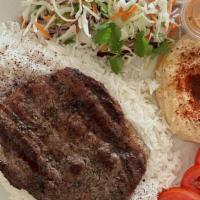 Rib-Eye Steak Plate · Marinated rib-eye steak served on a bed of rice, sides of salad, hummus, and pita bread.