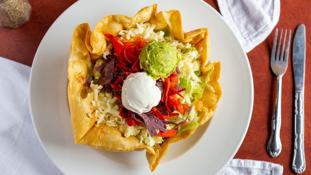 Taco Salad Cazuela · A bowl-shaped flour tortilla deep-fried and filled with picadillo, ground beef or chicken, refried beans, lettuce, shredded cheese, and tomato. Topped with tortilla strips, guacamole and sour cream.