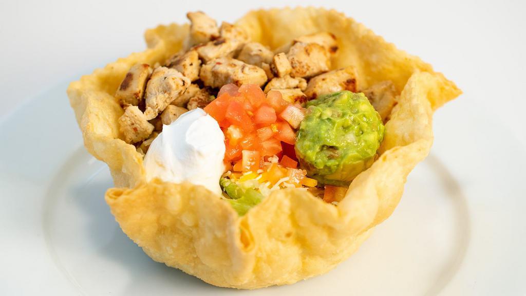 Grilled Chicken Taco Salad · Start with a fried flour tortilla then we add whole beans, shredded lettuce, cheddar- jack cheese, diced tomato, grilled chicken and finish it with sour cream and guacamole