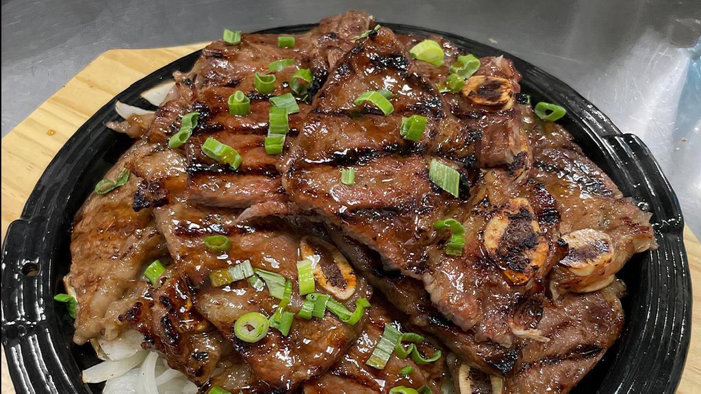 Korean Bbq Short Ribs · Beef short ribs marinated in Korean BBQ sauce, served on a bed of grilled onions, topped with green onions, comes with rice and pickled veggies
