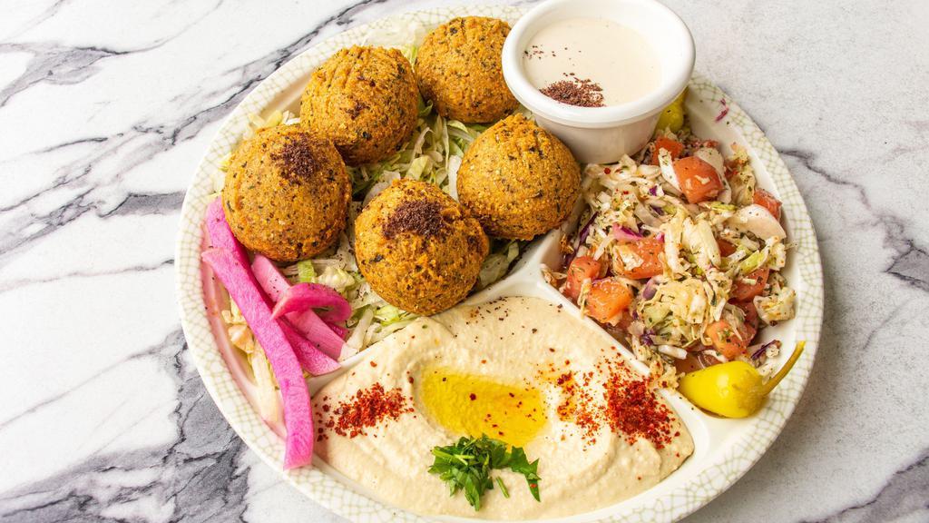 Falafel Plate · Vegan. Five pieces of falafel are served with hummus, tahini, lettuce, tomato, pickles, and pita bread.