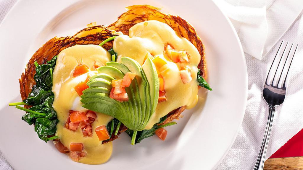Veggie Eggs Benedict · Two poached eggs on an English muffin, topped with tomato, spinach, and avocado, covered with hollandaise sauce. Served with choice of potatoes or fruit.