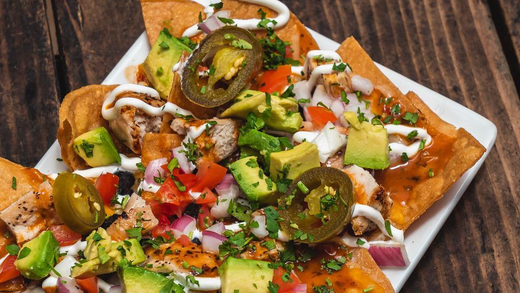 Grilled Chicken Nachos · Black beans, avocado, tomatoes, cilantro, red onions, cheese blend, sliced jalapenos, chipotle sauce, and crema.