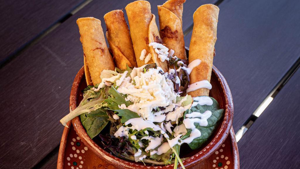 Mexicali Taquitos · 6 crispy taquitos (3 Chicken - 3 Beef) served with a tangy tomatillo chicken broth, greens, queso cotija, avocado salsa and roasted carrots & zucchini.