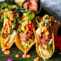 Vegan Tacos · Three plant-based meat tacos with cabbage, pico de gallo, and avocado on corn tortillas.