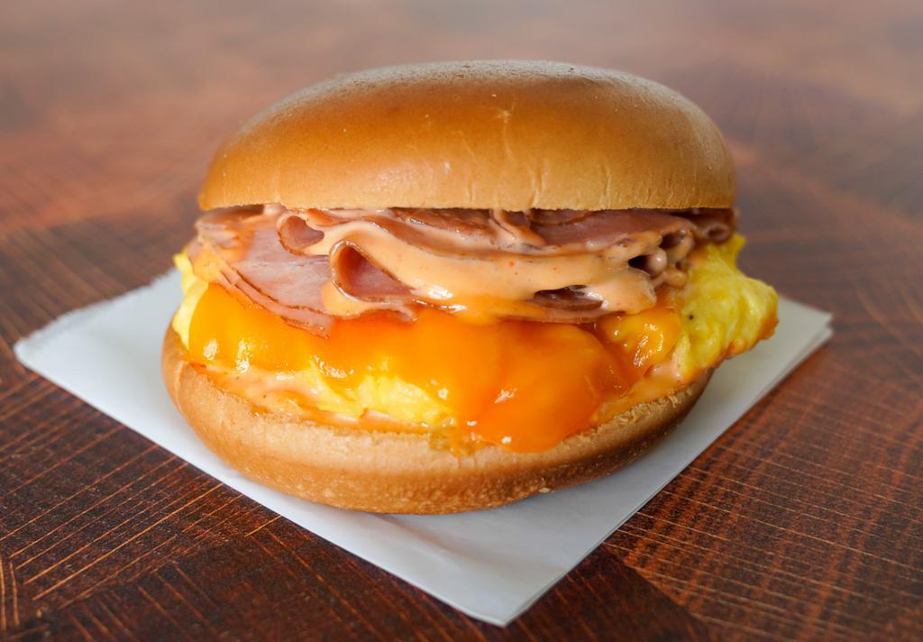 Brioche, Ham, Egg, & Cheddar Sandwich · 2 scrambled eggs, melted Cheddar cheese, sliced ham, and Sriracha aioli on a warm brioche bun.