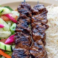 1B Beef Kebab · Skewered chunks of tender marinated beef, grilled to perfection. Served with rice, salad, hu...