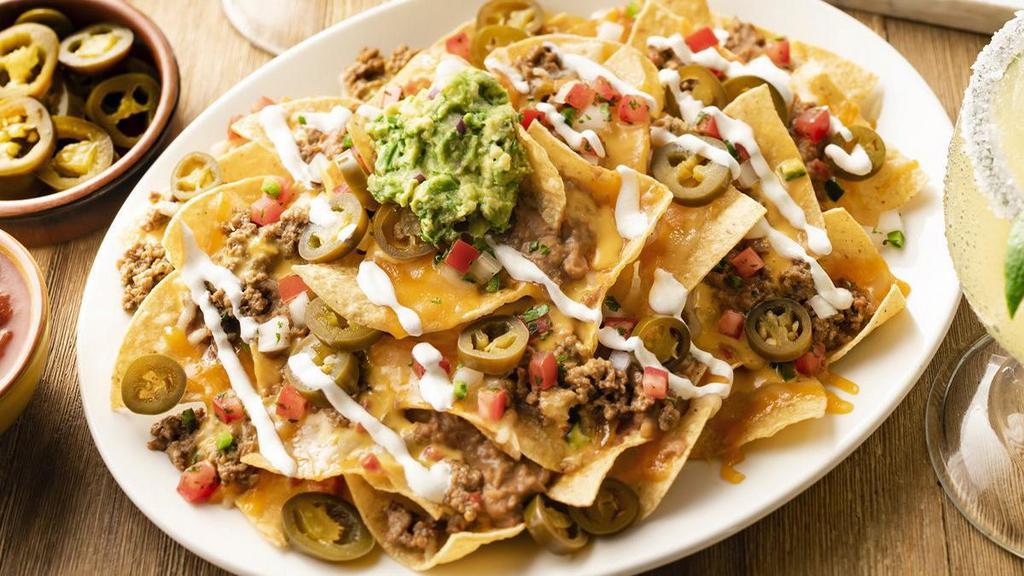 Stacked Nachos · Chips piled high with seasoned ground beef, refried beans and queso. Topped with lime crema, pico de gallo, pickled jalapeños and guacamole.