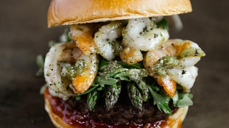 Surf & Turf Burger With Shrimp · Beef burger, topped with garlic jumbo shrimp (4) , roasted garlic butter, sweet chili sauce, grilled asparagus tips, tomato