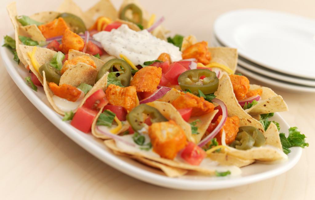 Buffalo Chicken Nachos · Tortilla chips with chicken tossed in our Buffalo Hot sauce, lettuce, tomatoes, red onions, fresh jalapeños, queso blanco, Cheddar Jack and served with our famous Bleu Cheese Dip.
