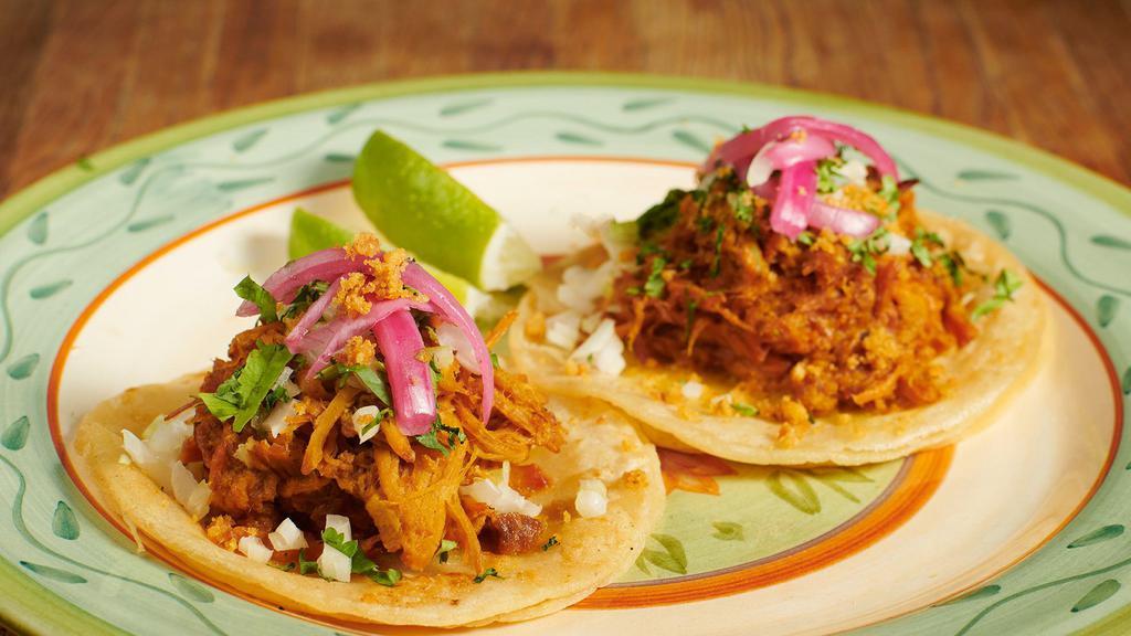 Cochinita Pibil Tacos · Two slow-roasted pork tacos topped with achiote, pickled onions, and cilantro.