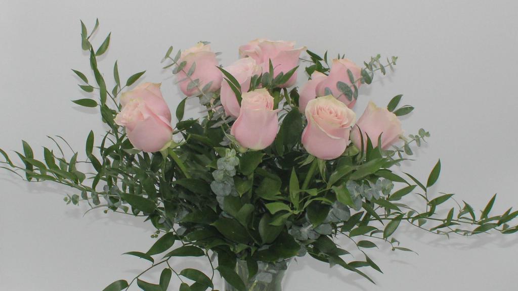 Dozen Pink Roses Vase Arrangement · A classic dozen pink roses with babies breath and greenery, arranged in a clear glass vase. The deluxe design includes upscale greens such as ruscus and eucalyptus instead of babies breath. Includes pink roses, baker fern, salal, gypsophila.
