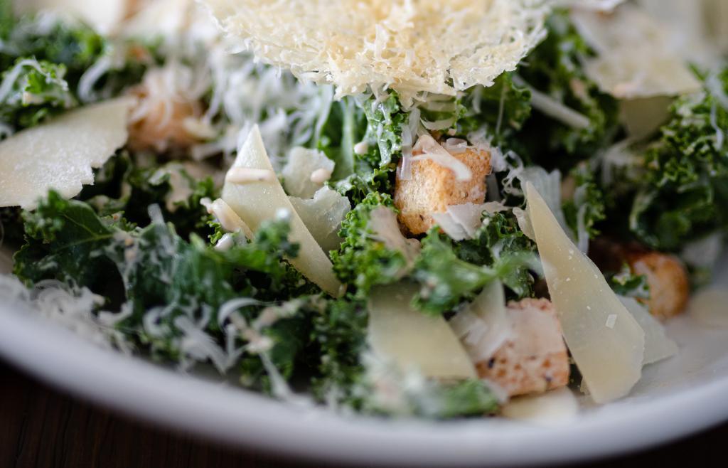 Kale Caesar Salad · Shaved aged parmesan crisp and crispy kale, tossed in a creamy caesar dressing topped with croutons.