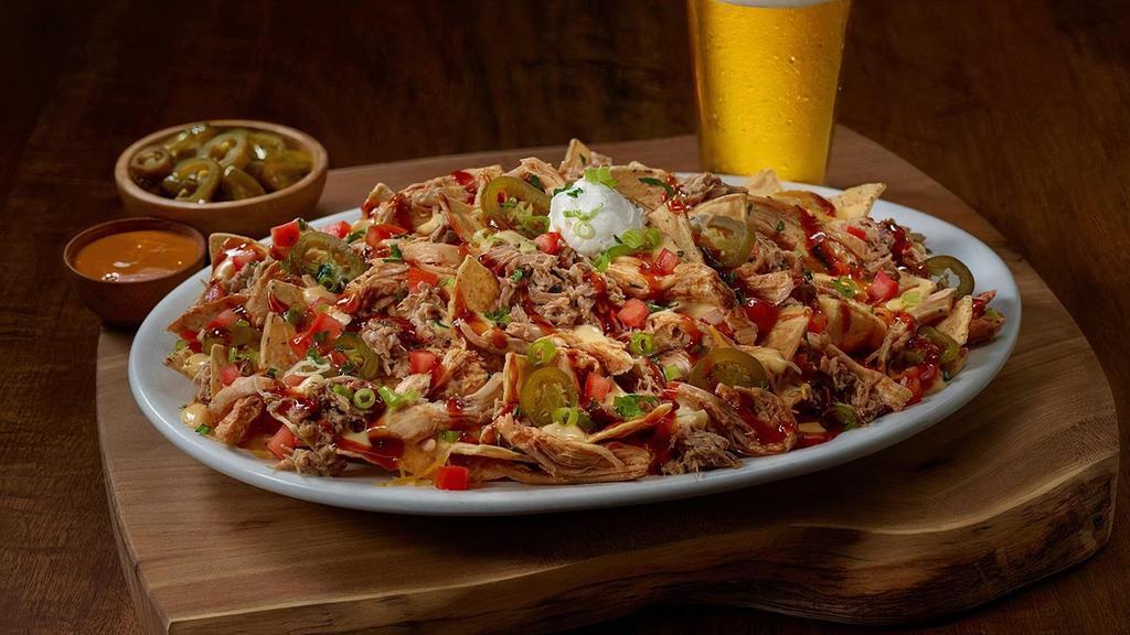 The Bbq Mag-Nacho · Loaded BBQ Mag-Nachos! Freshly fried tortilla chips topped with BBQ pulled chicken, hickory smoked, hand pulled pork, house-made queso, cheddar jack cheese, tomatoes, sliced jalapeños, green onions, sour cream, sweet BBQ glaze, and cilantro.