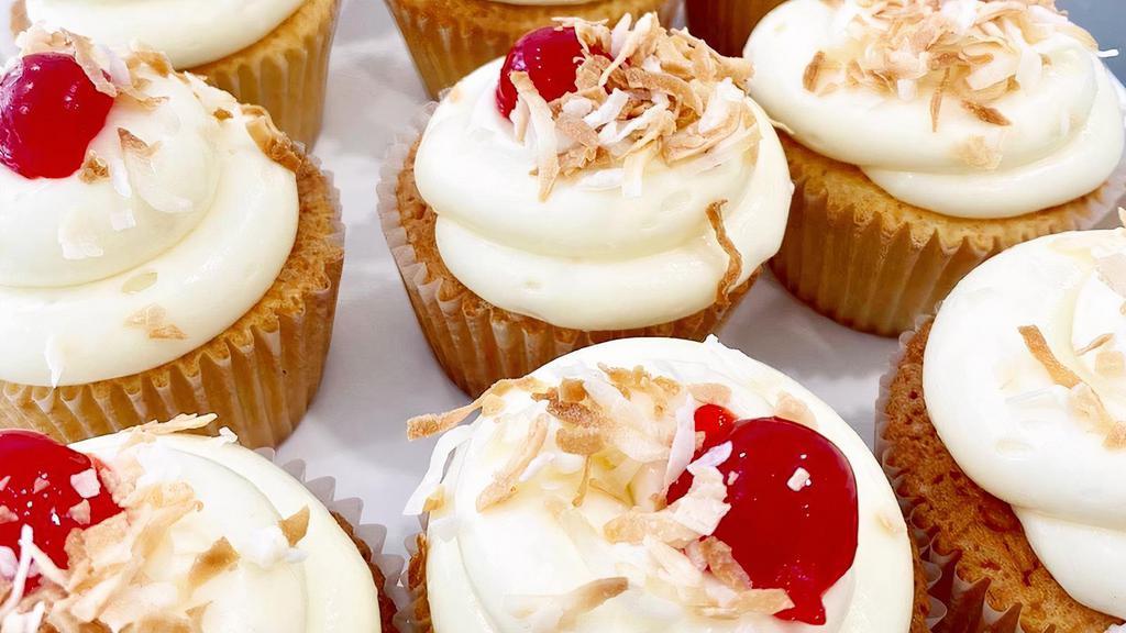 Piña Colada · Vanilla cake filled with pineapple, topped with coconut cream cheese frosting, toasted coconut flakes & a cherry on top.