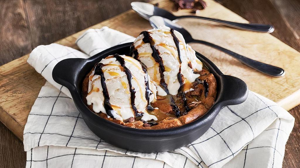 Chocolate Chip Cookie Skillet · A freshly baked chocolate chip cookie served warm in a skillet with vanilla bean ice cream and drizzled with caramel and chocolate sauces. It’s enough to share… or not!