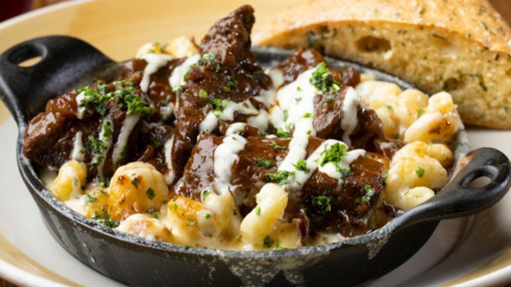 Short Rib Mac & Cheese · Tender and juicy boneless short ribs braised with caramelized onions and red wine sauce, drizzled with horseradish sour cream over a skillet of creamy cavatappi Mac & Cheese. Served with warm Rustic Bread.