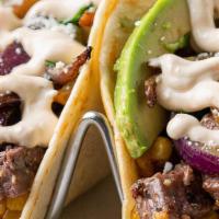 Grilled Steak & Avocado Taco · This meaty taco features sliced marinated skirt steak on a bed of roasted poblano corn medle...