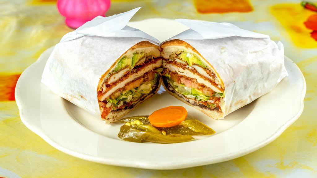 Milanesa De Res Torta · Beef Milanese with spread of beans, melted cheese, onions, avocado, lettuce, tomatoes, and jalapeno.
