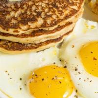 Buttermilk Pancakes With Eggs · Warm buttermilk pancakes served in stack of three with side of butter, syrup and fresh eggs.