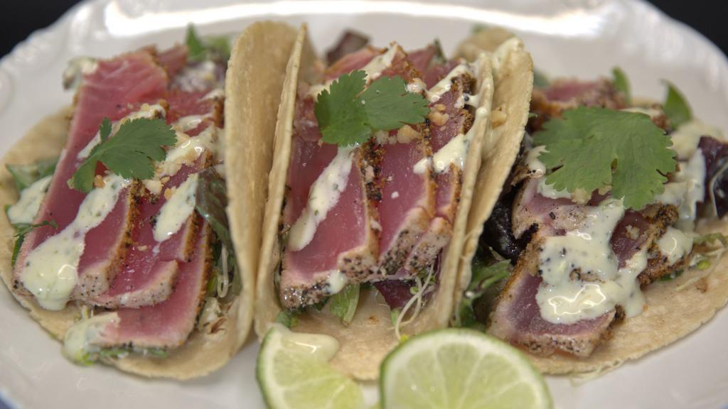 Seared Ahi Tacos (3 Pack) · Seared Ahi, Sliced and served over organic greens, cilantro, macadamia nuts, and feta cheese. Comes Sauced With our Signature Wasabi lime crema sauce and stone ground tortillas.