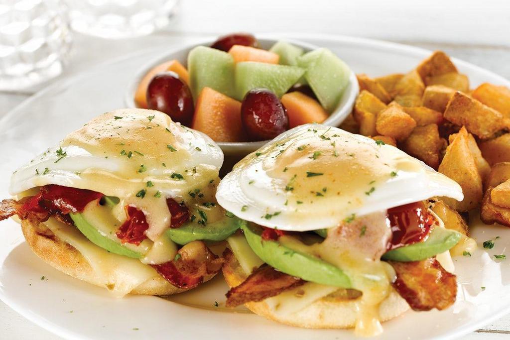 California Avocado Benedict · Two basted eggs*, fresh avocado, Applewood smoked bacon, oven-roasted tomatoes, Pepper Jack cheese, creamy hollandaise and garlic seasoning atop an English muffin. Served with fresh fruit and choice of cripsy hash browns or breakfast potatoes. .