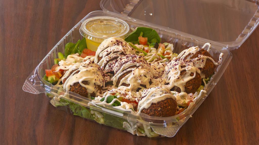 Falafel Salad · Flavorful, fresh greens that include: baby spinach, Romaine lettuce, tossed with our famous house salad (cucumber, tomatoes, onions), then topped with five-pieces of crispy falafel, covered with garlic sauce, olive oil, white vinegar, and shredded garlic.  Each bite is crisp, bright, and bursting with flavor.