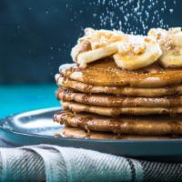 Buttermilk Pancakes With Fresh Bananas · 3 fluffy golden pancakes topped with fresh bananas and served with a side of syrup and butter.