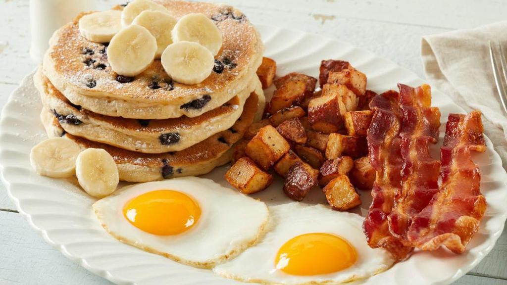 Banana Berry Farmer · Choice of premium breakfast meat with two fresh-cracked eggs* cooked-to-order and your choice of hash browns, home fries or fresh-cut fruit. Served with three blueberry hotcakes topped with fresh bananas
