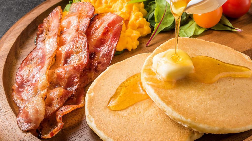 Bacon Buttermilk Pancakes · 3 perfectly fluffy pancakes topped with crispy bacon, served with a side of butter and syrup.
