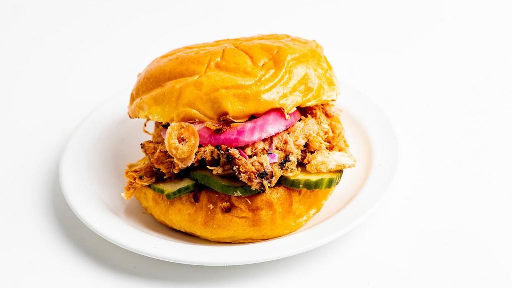 Pulled Chicken Sandwich · Served on a brioche bun with pickles, cabbage, pickled onions, crispy onions, a side of slaw and accompanied by one side with your choice of sauce and toppings.