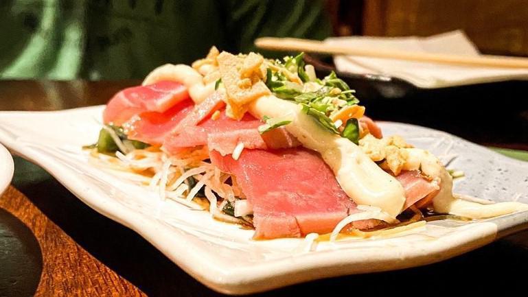 Doraku Tuna Tataki · Seared tuna served over a wakame daikon salad, garnished with garlic aioli and ponzu sauce.