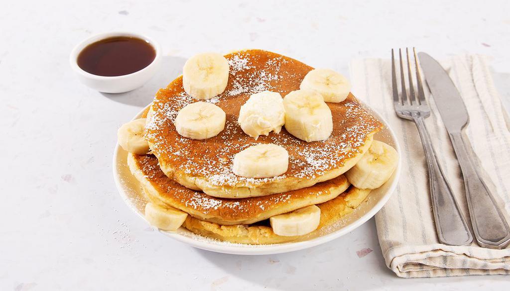 Banana Pancakes · Three fluffy buttermilk pancakes topped with sliced bananas, and served with maple syrup and powdered sugar.