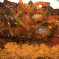 Churrasco Asado · Grilled skirt steak with onion and peppers. Plated with yellow rice and refried pinto beans.