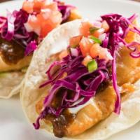 Crispy Salmon Tacos · Salmon dip in light tempura. Topped with guacamole, red cabbage, and sour cream. On a corn t...