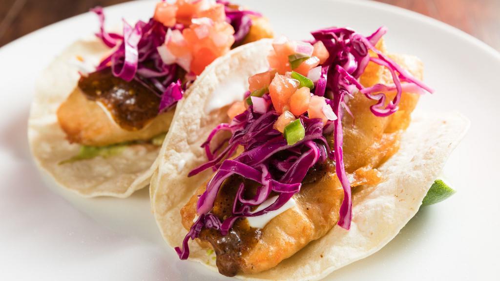 Crispy Salmon Tacos · Salmon dip in light tempura. Topped with guacamole, red cabbage, and sour cream. On a corn tortilla