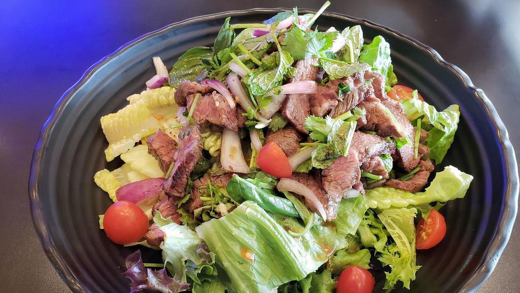 Thai Style Steak Salad · Sliced grilled steak tossed in thai dressing with mint, basil, red onions, chinese parsley, cherry tomatoes and cucumbers on romaine lettuce. Spicy.